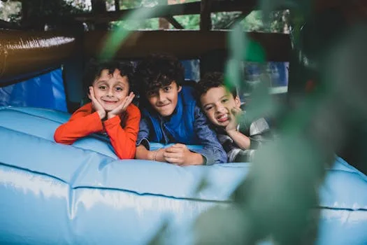 Three smiling children enjoy a bouncy time on a trampoline, embodying youthful joy and leisure in summer.